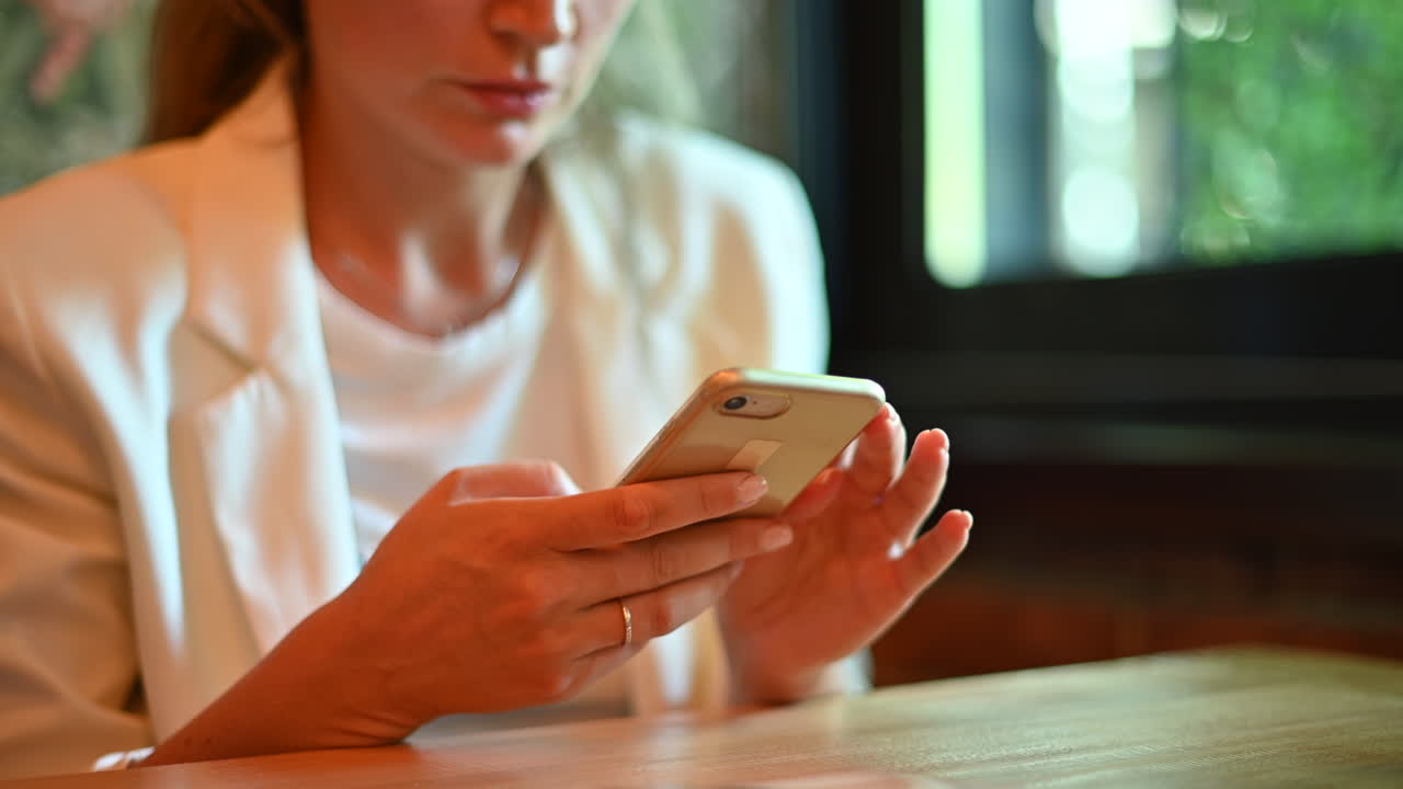 Donna vestita di bianco che chatta al cellulare a un tavolo in un bar