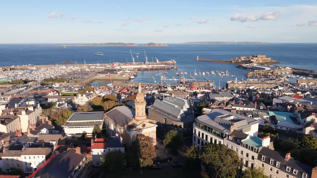 Flight over Elizabeth College St James and rooftops of St Peter Port Guernsey towards harbour Herm Sark and Jethou in the distance in bright afternoon sunshine on calm day