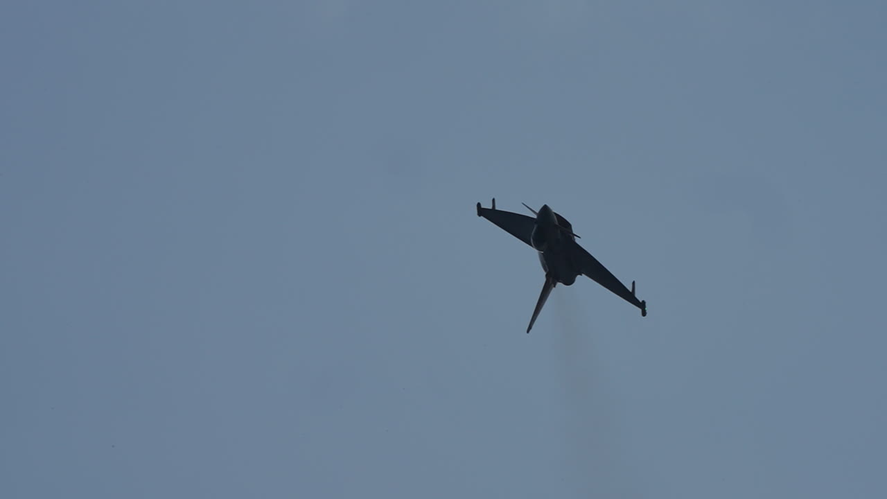 Military jet aircraft flying toward the camera and performing a twisting maneuver in slow motion against the sky
