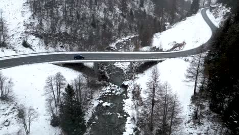 aerial view of a small car driving over a snow covered bridge on a cloudy winter day with snowfall in switzerland