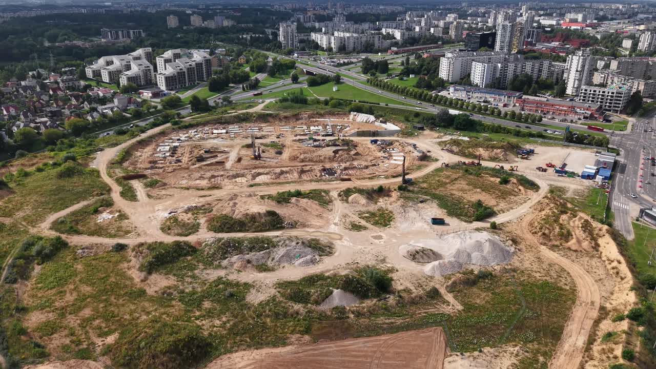 Vista aérea do canteiro de obras do Estádio Nacional de Vilnius, mostrando grandes trabalhos de terraplanagem e escavação. A silhueta da cidade ao fundo destaca o desenvolvimento urbano e a infraestrutura – 16 de agosto de 2025