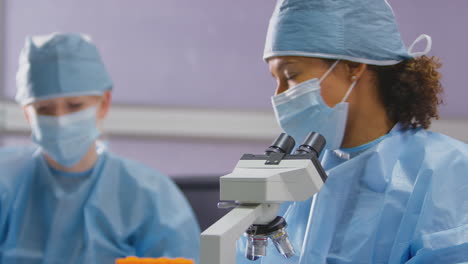 trabajadoras de laboratorio que usan ppe analizando muestras en el laboratorio con resultados de pruebas de registro al microscopio