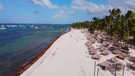 Playa-De-Arena-Llena-De-Tumbonas,-Botes-En-El-Mar-Caribe,-Bavaro-Resort-En-Punta-Cana,-República-Dominicana,-Vista-Aérea-De-Drones,-Vuelo-Bajo