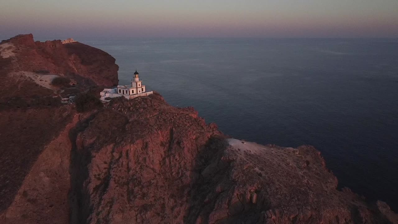 faro en la cima de un acantilado, al atardecer, en la isla de santorini