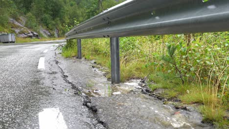 Stream-of-water-flowing-down-roadside-below-metal-road-fence-during-heavy-rain