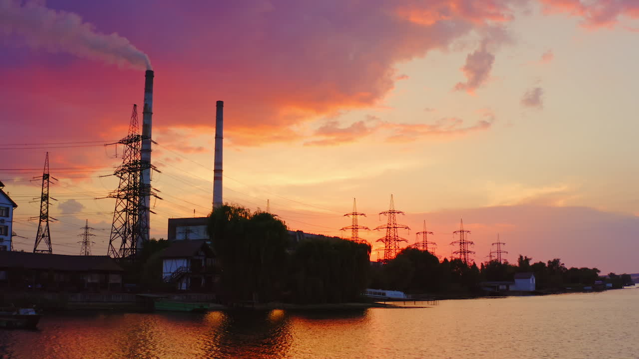 Manufacturing near the river. Industrial plant and high voltage electric towers among nature at sunset. View from the river. Aerial view.