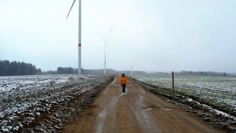 Beautiful-woman-walking-on-a-dirt-gravel-road-in-front-of-windmills