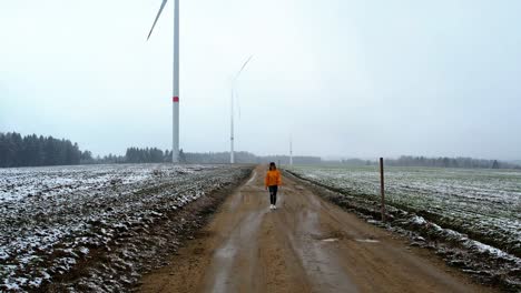 beautiful woman walking on a dirt gravel road in front of windmills