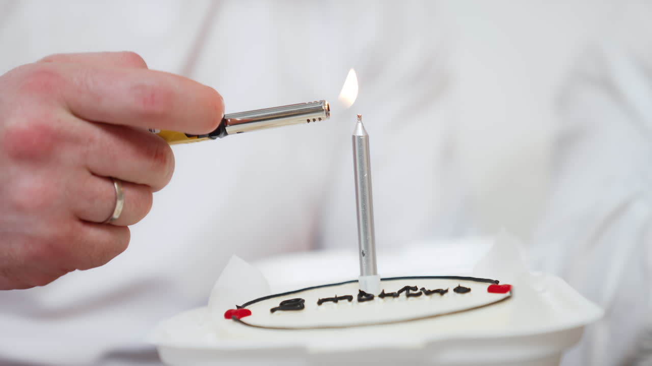 Male hand lights the candle in a cake. Celebration cake close up. White backdrop.
