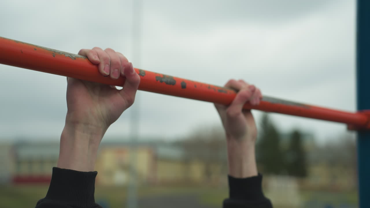Close-up of a boy working out on pull-up bars in an outdoor gym area, after successfully completing his fourth pull-up, he struggles to continue, with blur background