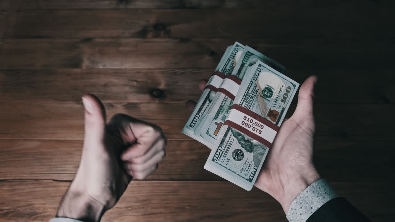 남자 손은 나무 바탕에 10,000 달러 지폐의 세 어리를 들고 있습니다.