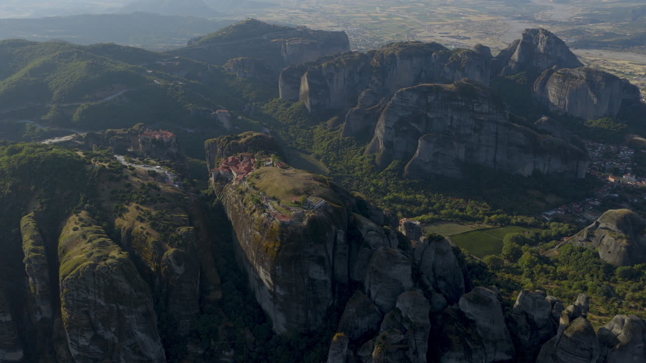 Cinematic aerial view of Meteora monastery in Greece perched on towering cliffs, dramatic rock formations and lush green valley create a breathtaking historic scene