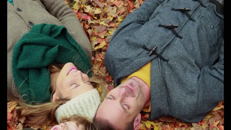 family lying on autumn leaves in park