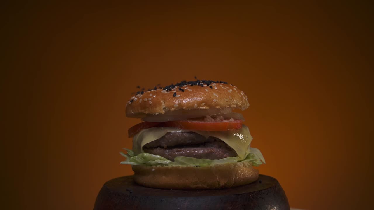lluvia de semillas cayendo sobre una hamburguesa en una base de madera con fondo naranja