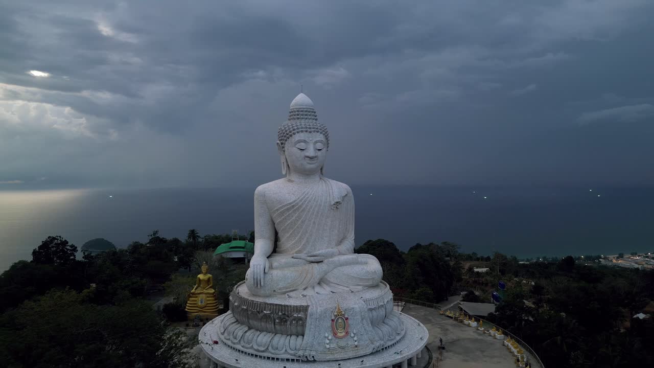 Aerial view of the Big Buddha in Phuket, Thailand at dusk, with dramatic clouds and the Andaman Sea in the background