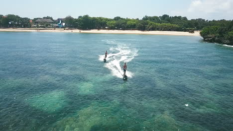 Two-young-adventurous-people-riding-jetsurf-boards-through-calm-clear-waters-of-tropical-Bali,-slow-motion