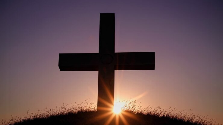 Silhouette di una croce su una collina al tramonto, ripresa da un angolo basso