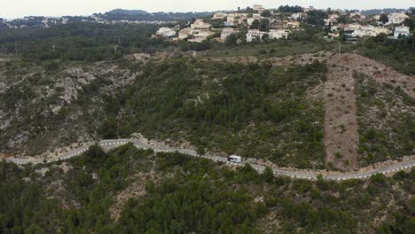 Aerial-shot-of-a-campervan-or-motorhome-on-a-hillside-road-in-the-seaside-town-of-Jávea,-Spain,-on-a-cloudy-day