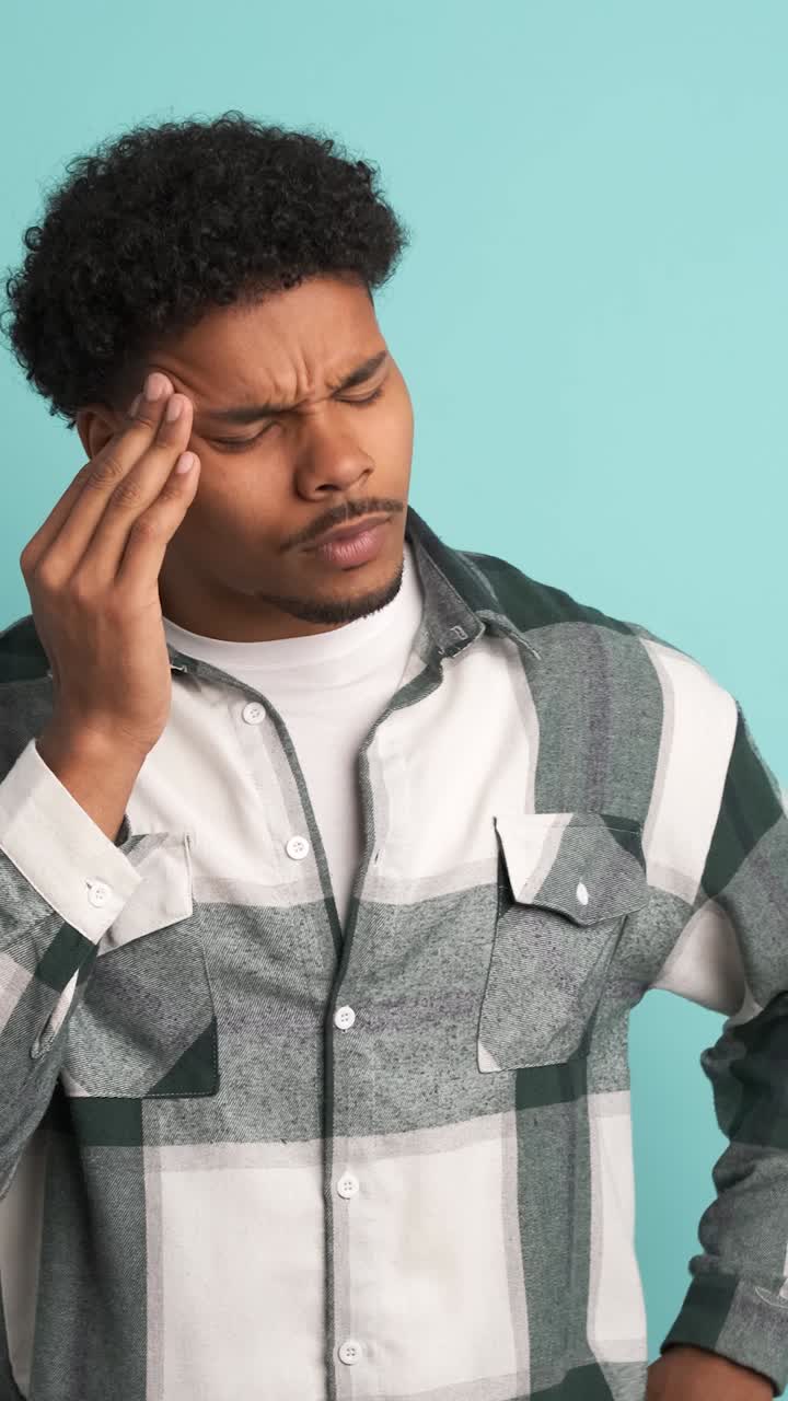 Frustrated man suffering from headache in blue studio