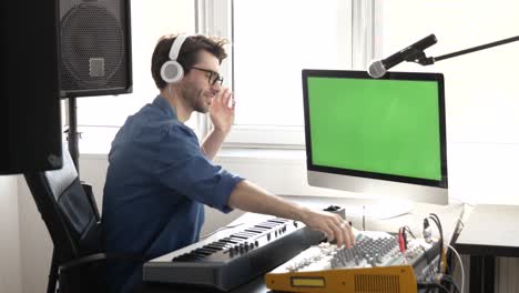 joven en el estudio de grabación de sonido. usando y ajustando el mezclador de la consola y disfrutando escuchando música en auriculares. gran pantalla verde.