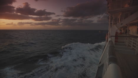 cruise ship sailing on a calm see with high speed while at the horizon the colors of a sunset are visible on a partly cloudy day. slowmo wide shot