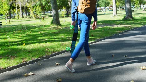 mujer con patineta caminando por la calle cerca del parque 4k