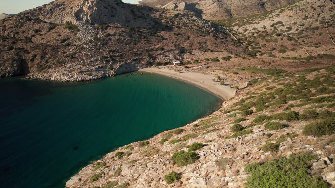 descenso aéreo a lo largo de las rocosas colinas de acantilados de textura áspera a la pacífica playa de arena dorada y el agua clara, varvarousa syros grecia