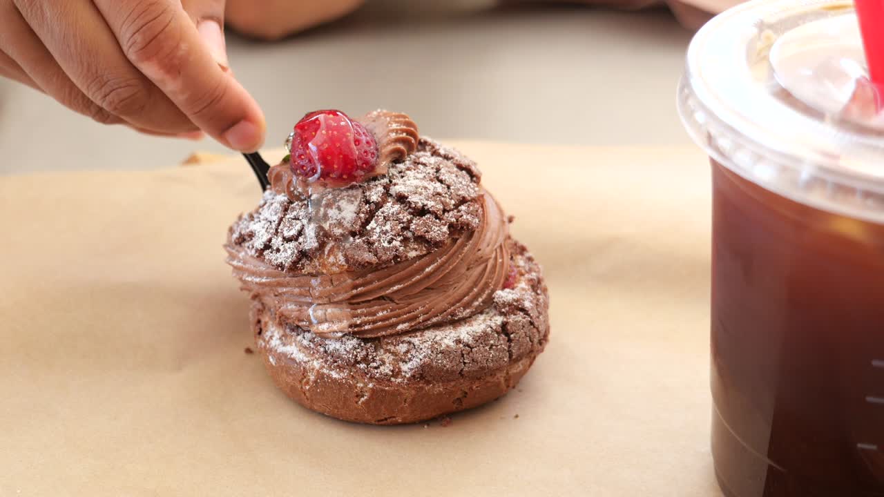 Person eating a chocolate strawberry cream puff with coffee