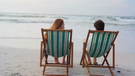 rear view of young caucasian couple relaxing on sun lounger at beach on a sunny day 4k