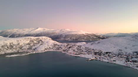 ersfjordvegen village surrounded by snow-capped mountains during golden hour, aerial view