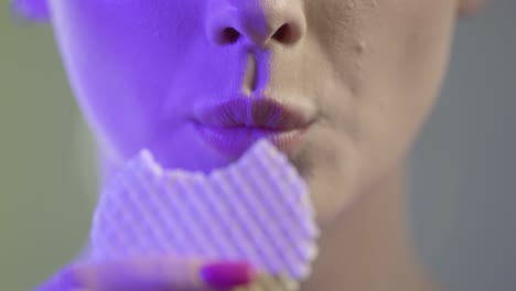 close up of woman's face and mouth, eating and chewing wafer, colorful studio lighting