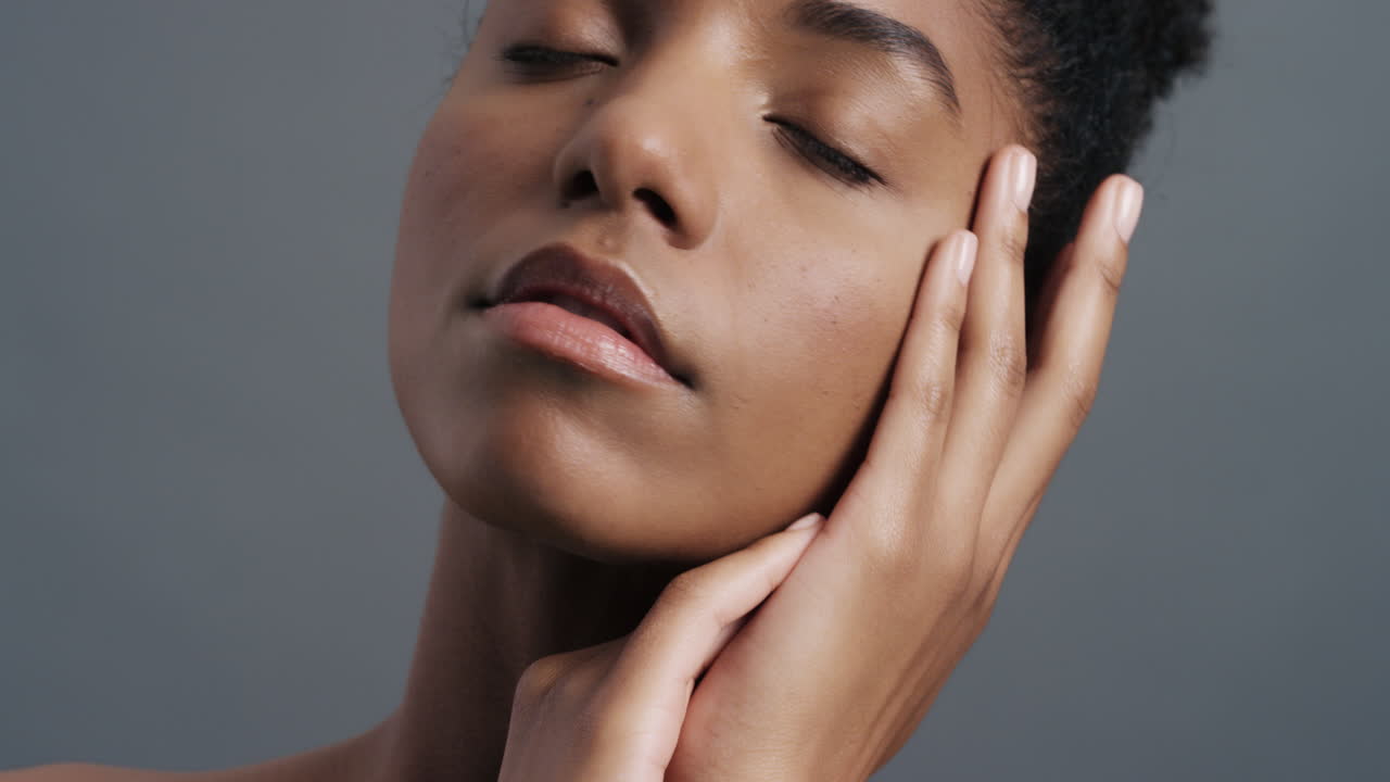 retrato en primer plano de una hermosa mujer afroamericana tocando suavemente la cara con las manos disfrutando de una piel suave y saludable, un cutis de belleza femenina natural, un concepto de cuidado de la piel