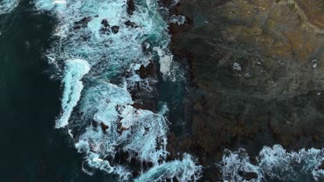 Top-down-drone-shot-of-waves-crashing-onto-California's-rocky-coastline