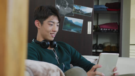 Asian-boy-using-digital-tablet-sitting-on-the-couch-at-home