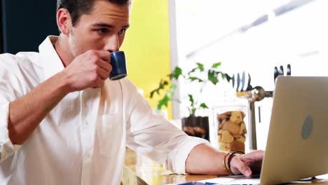 cliente masculino usando computadora portátil mientras toma café en el mostrador