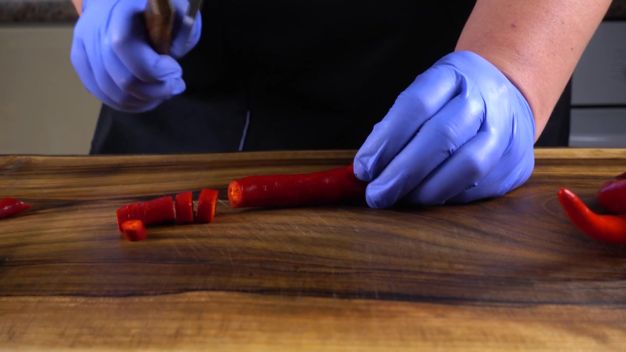 The cook cuts chilli pepper on a cutting board.