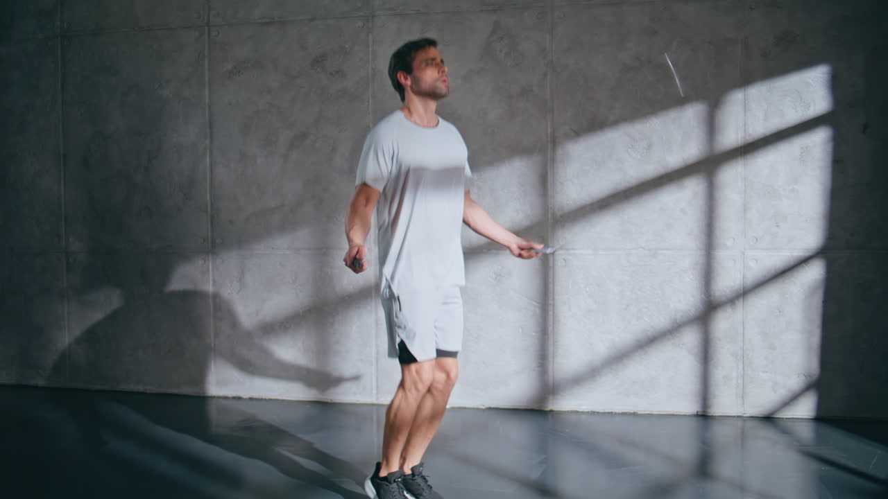 Strong man doing cardio workout with jump rope at loft room. Sportsman jumping