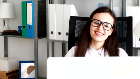 mujer de negocios bebiendo café y sonriendo ante la computadora portátil en una oficina moderna