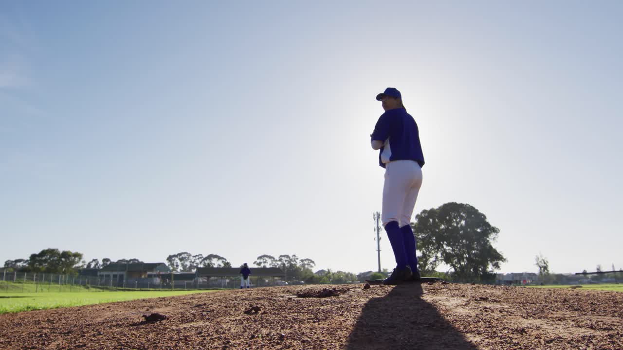 Giocatrice di baseball caucasica con gli occhiali che lancia la palla su un campo da baseball soleggiato.