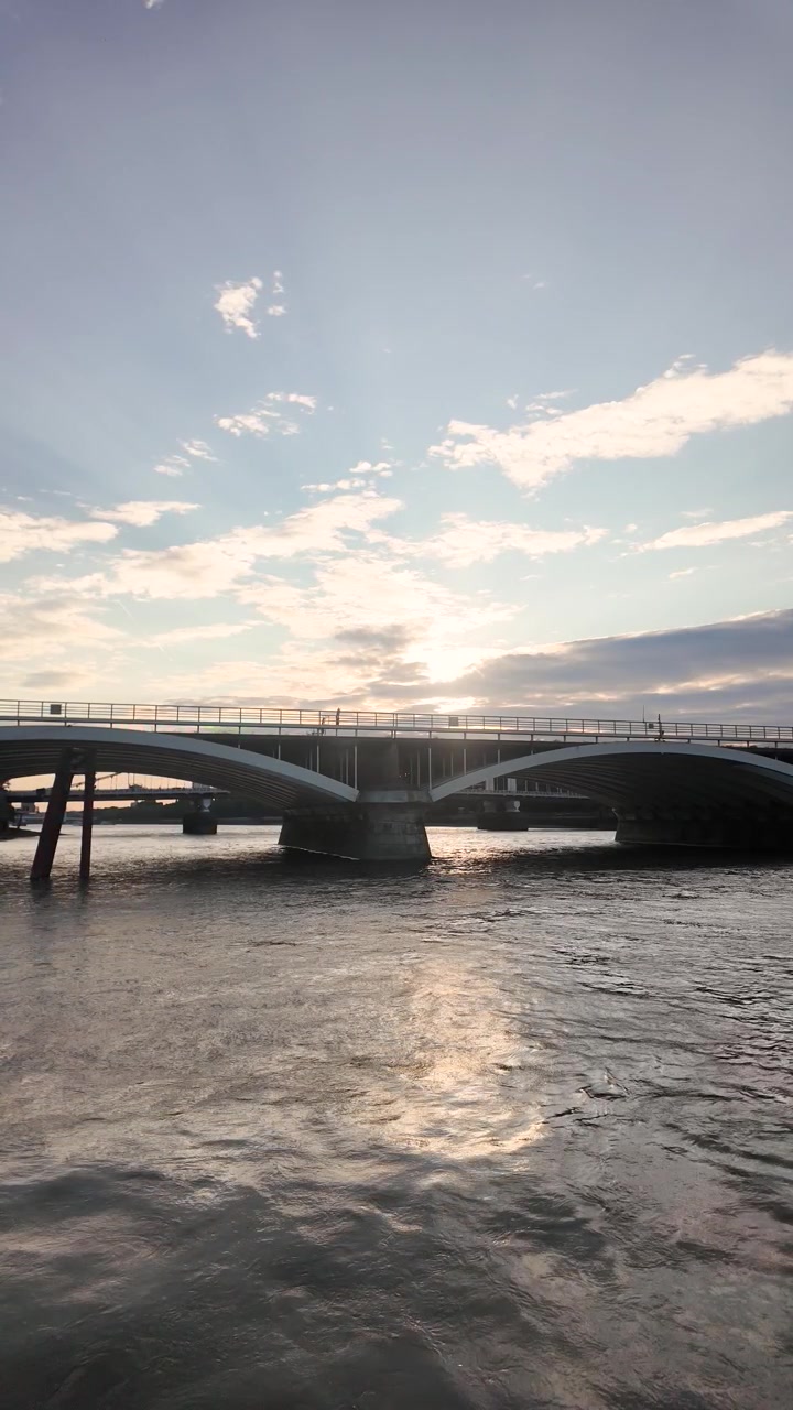 Il Ponte Grosvenor attraversa il Tamigi mentre il bagliore del sole basso si increspa sull'acqua in movimento. Video verticale, rallentatore