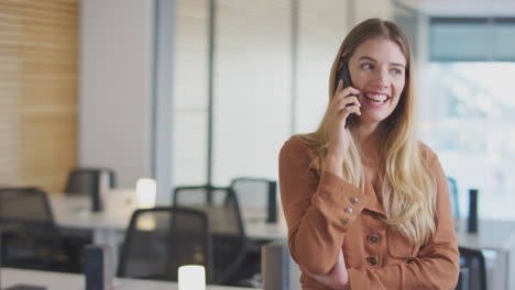 Smiling-Businesswoman-On-Phone-Call-Standing-In-Modern-Open-Plan-Office