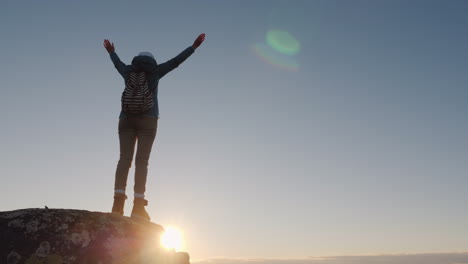 a successful woman traveler at the top of the mountain raises her hands up reach the top of the conc