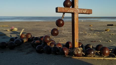 a cross wrapped in rosary beads sits on a beautiful beach with waves in the background