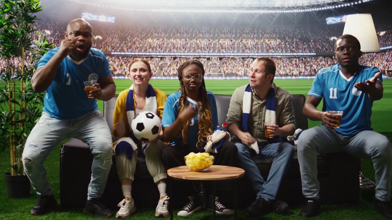 Grupo de amigos siguiendo un partido de fútbol en casa con una transmisión inmersiva.
