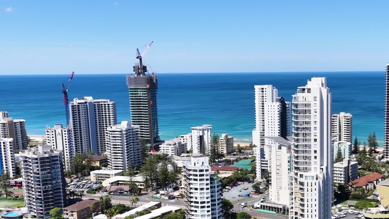 Daytime drone ascends above Broadbeach Waters, revealing coastal skyscrapers, blue ocean, and clear sky