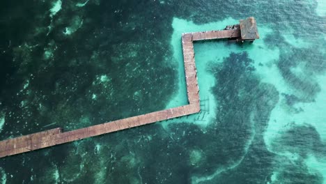 Wooden-boardwalk-without-railing-in-tropical-ocean-with-sandy-coral-below-clear-tropical-water