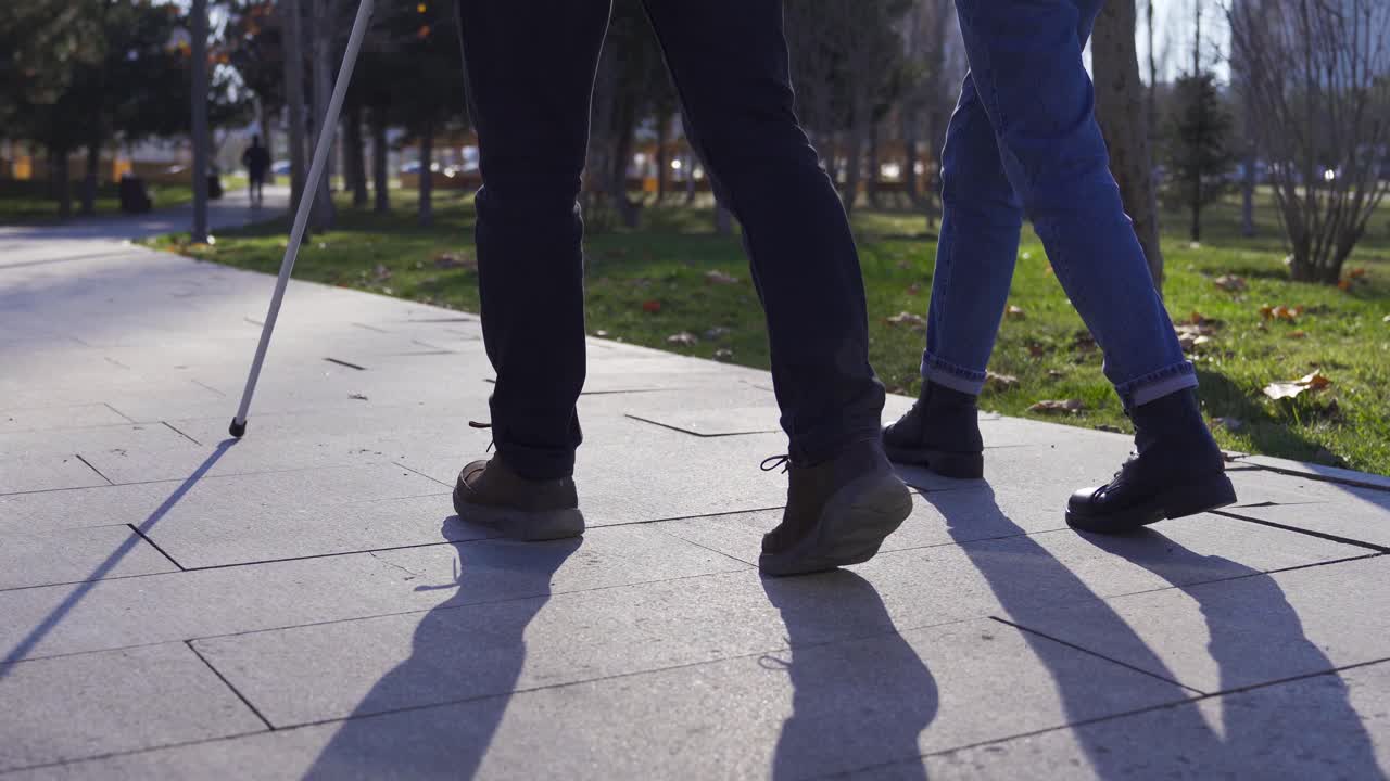 Close-up of blind man's cane and feet walking on the road with his wife.