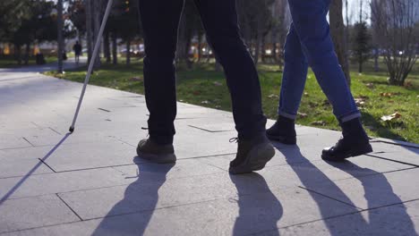 close-up of blind man's cane and feet walking on the road with his wife.