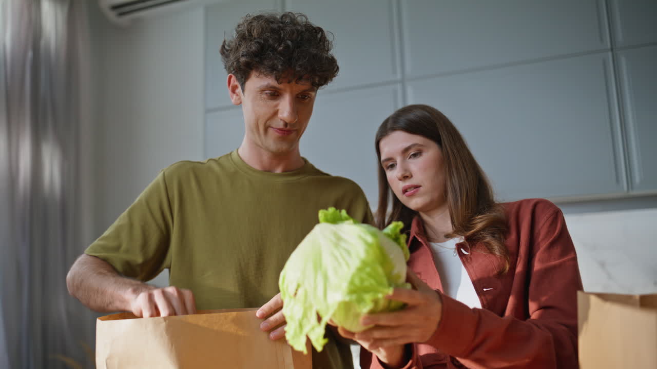 Couple unpacking delivered products talking at kitchen closeup. Laughing pair
