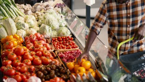 Product-review-A-man-with-a-Black-skin-color-in-a-plaid-shirt-chooses-vegetables-on-a-supermarket-counter.-View-of-juicy-and-rich-summer-vegetables